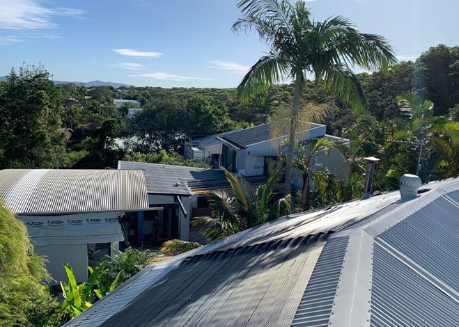 View from a rooftop overlooking a tropical residential area with modern houses surrounded by lush greenery and tall palm trees under a sunny, clear blue sky – perfect for your landing page or showcasing high-quality pool covers. | AES Pool Heating Solutions